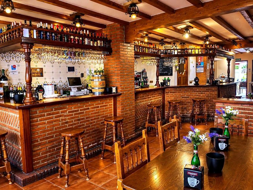 El interior del bar La Plaza, con la barra de ladrillo, las copas colgadas y los taburetes