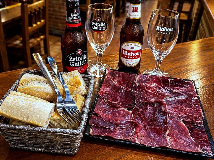 Mesa del bar La Plaza con cecina de León cortada fina, cesta de pan y dos cervezas bien frías